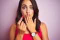 Young beautiful woman applying red lipstick over pink isolated background cover mouth with hand shocked with shame for mistake, Royalty Free Stock Photo