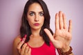 Young beautiful woman applying red lipstick over pink isolated background with open hand doing stop sign with serious and Royalty Free Stock Photo