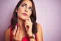 Young beautiful woman applying red lipstick over pink isolated background serious face thinking about question, very confused idea Royalty Free Stock Photo