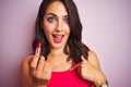 Young beautiful woman applying red lipstick over pink isolated background with surprise face pointing finger to himself Royalty Free Stock Photo