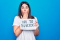 Young beautiful woman asking for psychical problem holding paper with not to suicide message covering mouth with hand, shocked and