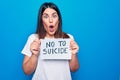 Young beautiful woman asking for psychical problem holding paper with not to suicide message scared and amazed with open mouth for Royalty Free Stock Photo