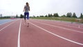 A young beautiful woman athlete in red snikers start running and runs past the camera during a day running training at