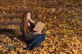 Young beautiful woman in autumn forest with book. Girl sitting on stairs in yellow leaves and reads book Royalty Free Stock Photo