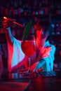 Young beautiful woman, bartender in modern bar, making delicious Aperol Spritz cocktail in neon, decorating with leaf