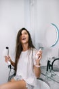 Young beautiful woman in the bathroom holding a hairdryer and a small bottle Royalty Free Stock Photo