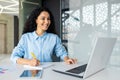Young beautiful woman behind paper work inside office, satisfied with achievement Hispanic woman sitting at workplace Royalty Free Stock Photo