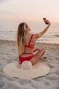 Young beautiful woman in bikini with straw hat sit and makes selfie at beach Royalty Free Stock Photo