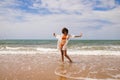 Young beautiful woman in bikini walking along the beach shore. The woman is enjoying her trip to a paradise beach while making Royalty Free Stock Photo