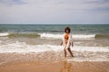 Young beautiful woman in bikini walking along the beach shore. The woman is enjoying her trip to a paradise beach while making Royalty Free Stock Photo