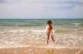 Young beautiful woman in bikini walking along the beach shore. The woman is enjoying her trip to a paradise beach while making Royalty Free Stock Photo