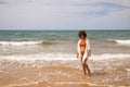 Young beautiful woman in bikini walking along the beach shore. The woman is enjoying her trip to a paradise beach while making Royalty Free Stock Photo