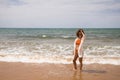Young beautiful woman in bikini walking along the beach shore. The woman is enjoying her trip to a paradise beach while making Royalty Free Stock Photo