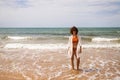 Young beautiful woman in bikini walking along the beach shore. The woman is enjoying her trip to a paradise beach while making Royalty Free Stock Photo