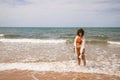 Young beautiful woman in bikini walking along the beach shore. The woman is enjoying her trip to a paradise beach while making Royalty Free Stock Photo