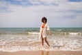 Young beautiful woman in bikini walking along the beach shore. The woman is enjoying her trip to a paradise beach while making Royalty Free Stock Photo