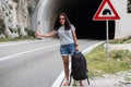 Young beautiful woman with black backpack hitchhiking standing near the road tunnel. Royalty Free Stock Photo