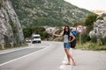 Young beautiful woman with black backpack hitchhiking standing on road. Beautiful young female hitchhiker by the road during vacat Royalty Free Stock Photo