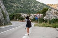 Young beautiful woman with black backpack hitchhiking standing on road. Beautiful young female hitchhiker by the road during vacat Royalty Free Stock Photo