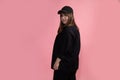 Young beautiful woman in black casual clothes and sports baseball cap stands with back half-sided to camera and looks into frame Royalty Free Stock Photo