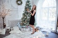 Young beautiful woman in black elegant evening dress standing on floor near christmas tree and presents on a new year eve. Royalty Free Stock Photo