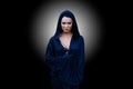 Young beautiful woman with a black hair and in the dark blue cloak with hood at the black background Royalty Free Stock Photo