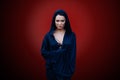 Young beautiful woman with a black hair and in the dark blue cloak with hood at the red background Royalty Free Stock Photo