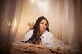 Young beautiful woman in black lace and white shirt in boudoir room lying on a bed near white transparent tulle curtains Royalty Free Stock Photo