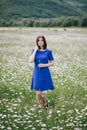 Young beautiful woman in a blue dress enjoying chamomile field among mountains