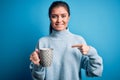 Young beautiful woman with blue eyes drinking mug of coffee over isolated background with surprise face pointing finger to himself Royalty Free Stock Photo