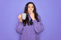 Young beautiful woman with blue eyes drinking mug of coffee over isolated purple background cover mouth with hand shocked with Royalty Free Stock Photo