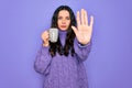 Young beautiful woman with blue eyes drinking mug of coffee over isolated purple background with open hand doing stop sign with Royalty Free Stock Photo