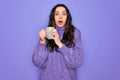 Young beautiful woman with blue eyes drinking mug of coffee over isolated purple background scared in shock with a surprise face, Royalty Free Stock Photo