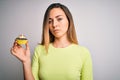 Young beautiful woman with blue eyes eating sweet chocolate cupcake over white background with a confident expression on smart