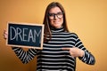 Young beautiful woman with blue eyes holding blackboard with dream message word with surprise face pointing finger to himself