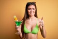 Young beautiful woman with blue eyes on vacation wearing bikini drinking cocktail happy with big smile doing ok sign, thumb up Royalty Free Stock Photo