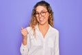 Young beautiful woman with blue eyes wearing casual shirt and glasses over purple background smiling with happy face looking and Royalty Free Stock Photo