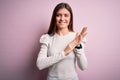 Young beautiful woman with blue eyes wearing casual white t-shirt over pink background clapping and applauding happy and joyful, Royalty Free Stock Photo