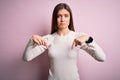 Young beautiful woman with blue eyes wearing casual white t-shirt over pink background Pointing down looking sad and upset, Royalty Free Stock Photo