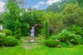 A young beautiful woman in a blue raincoat with a phone in garden park  on summer day with green bushes under blue sky. Tourism Royalty Free Stock Photo