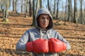 Young beautiful woman boxer in a tracksuit with a hood on his head in red boxing gloves trains in the forest in nature Royalty Free Stock Photo