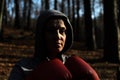 Young beautiful woman boxer in a tracksuit with a hood on his head in red boxing gloves trains in the forest in nature Royalty Free Stock Photo