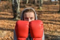 Young beautiful woman boxer in a tracksuit with a hood on his head in red boxing gloves trains in the forest in nature Royalty Free Stock Photo