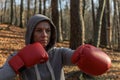 Young beautiful woman boxer in a tracksuit with a hood on his head in red boxing gloves trains in the forest in nature Royalty Free Stock Photo