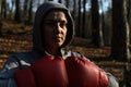 Young beautiful woman boxer in a tracksuit with a hood on his head in red boxing gloves trains in the forest in nature Royalty Free Stock Photo