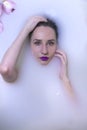 model girl with violet make-up in milk bath with violet flowers