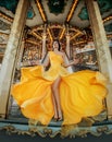 Young beautiful woman in a bright yellow evening dress posing against the backdrop of an amusement park and carousel