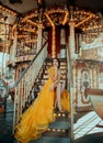 Young beautiful woman in a bright yellow evening dress sitting on stairs. Fashion model posing against the backdrop of Royalty Free Stock Photo