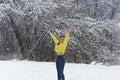 Young beautiful woman in bright yellow sweater rejoices  first snowfall, raising hands up. Lady in winter forest for walk,  first Royalty Free Stock Photo