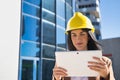 Young beautiful woman in brown coat, yellow workman`s helmet and blueprint tube, working with her tablet. Business concept, Royalty Free Stock Photo